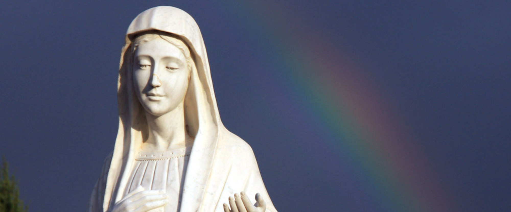 Bis zu einer Million Pilger besuchen jährlich den Wallfahrtsort Medjugorje. Bild: Marienstatue vor einem Regenbogen.